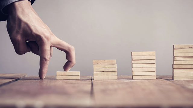 Hand of business man step up to a toy staircase to success target grow