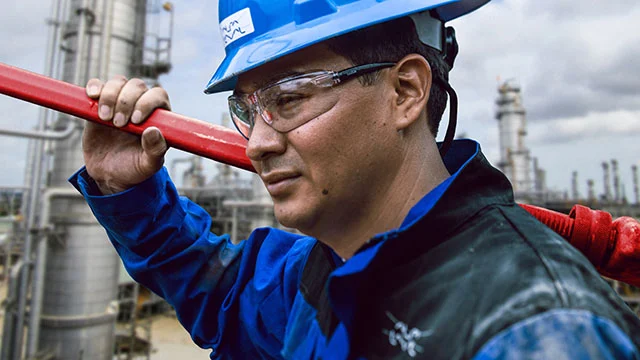 service man in front of plant holding red metal tool